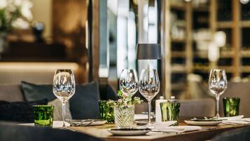 Una mesa de comedor dispuesta con copas de vino, platos y cristalería verde, con un interior moderno y un sofá al fondo.