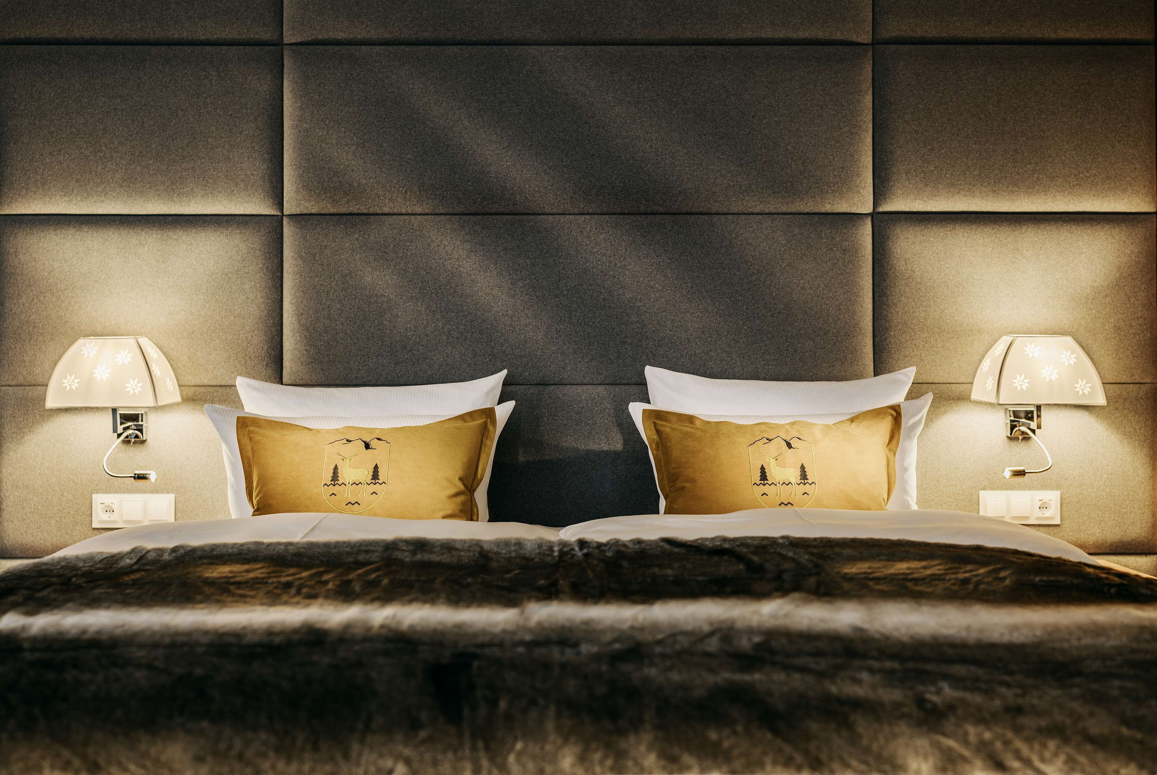 A hotel room with a tufted headboard, two bedside lamps, and a bed with a dark, furry throw blanket.