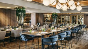 Un restaurante moderno con techos altos, iluminación colgante y diversas opciones de asientos, incluyendo taburetes y mesas.