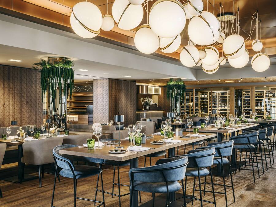 Un restaurante moderno con techos altos, iluminación colgante y diversas opciones de asientos, incluyendo taburetes y mesas.