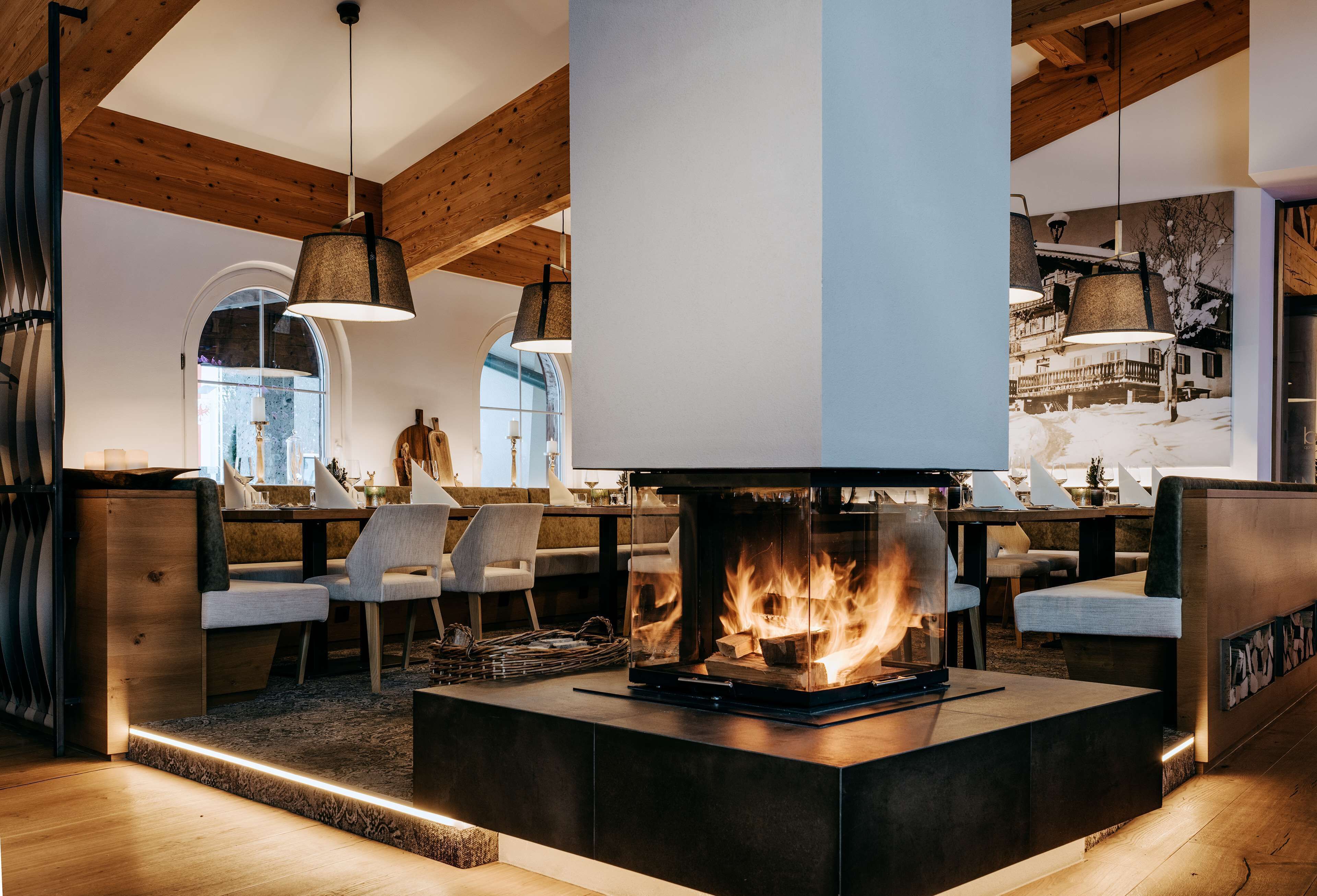 A modern interior with a central fireplace, wooden ceiling beams, and a seating area with chairs and tables.