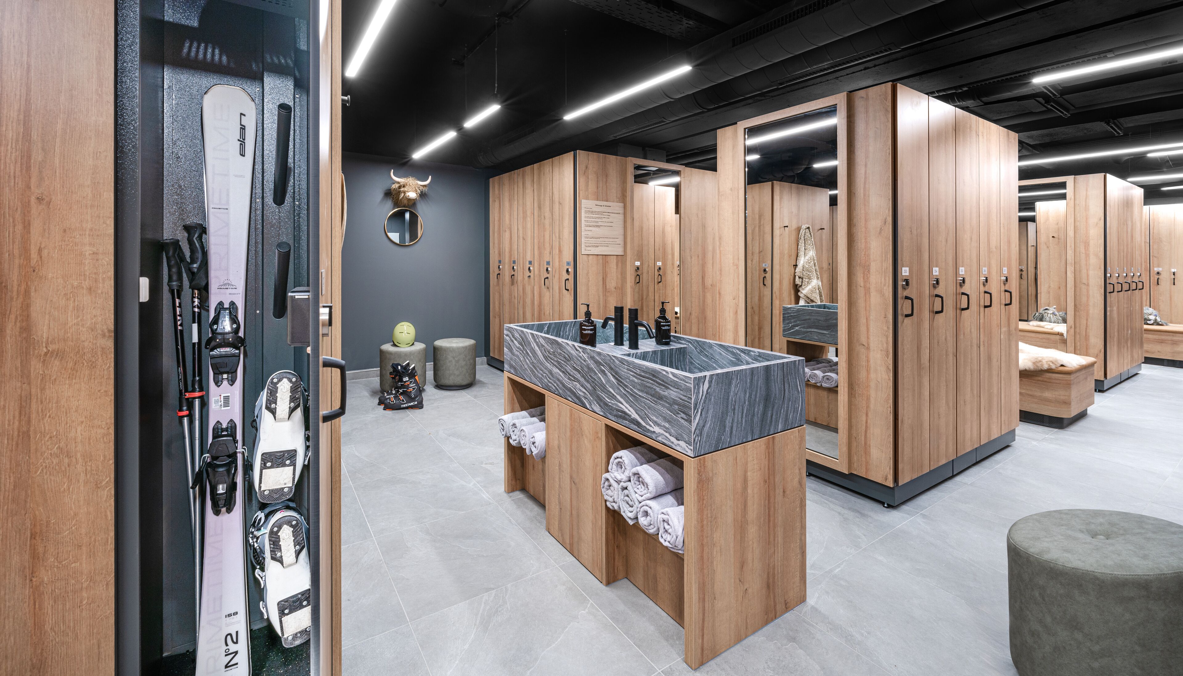 A modern locker room with wooden lockers, a marble sink, and ski equipment.