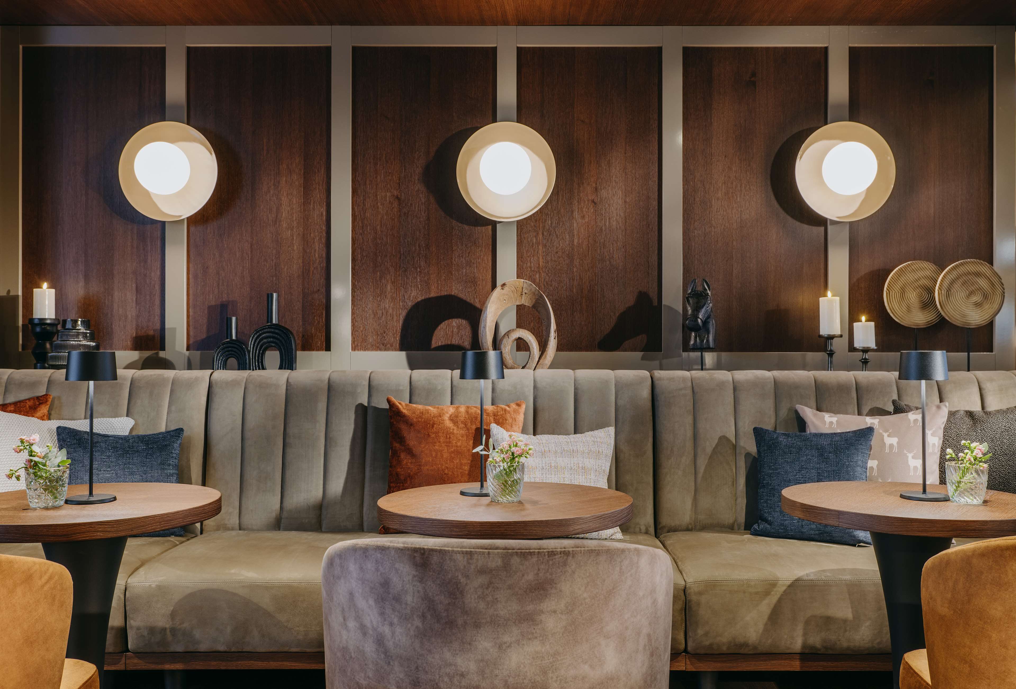 Un espace de détente moderne, avec un canapé, des tables rondes et des lampes fixées au mur.