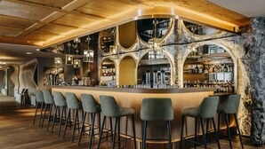 Zona de bar con una barra de madera curva, varios taburetes y un fondo de pared de piedra.