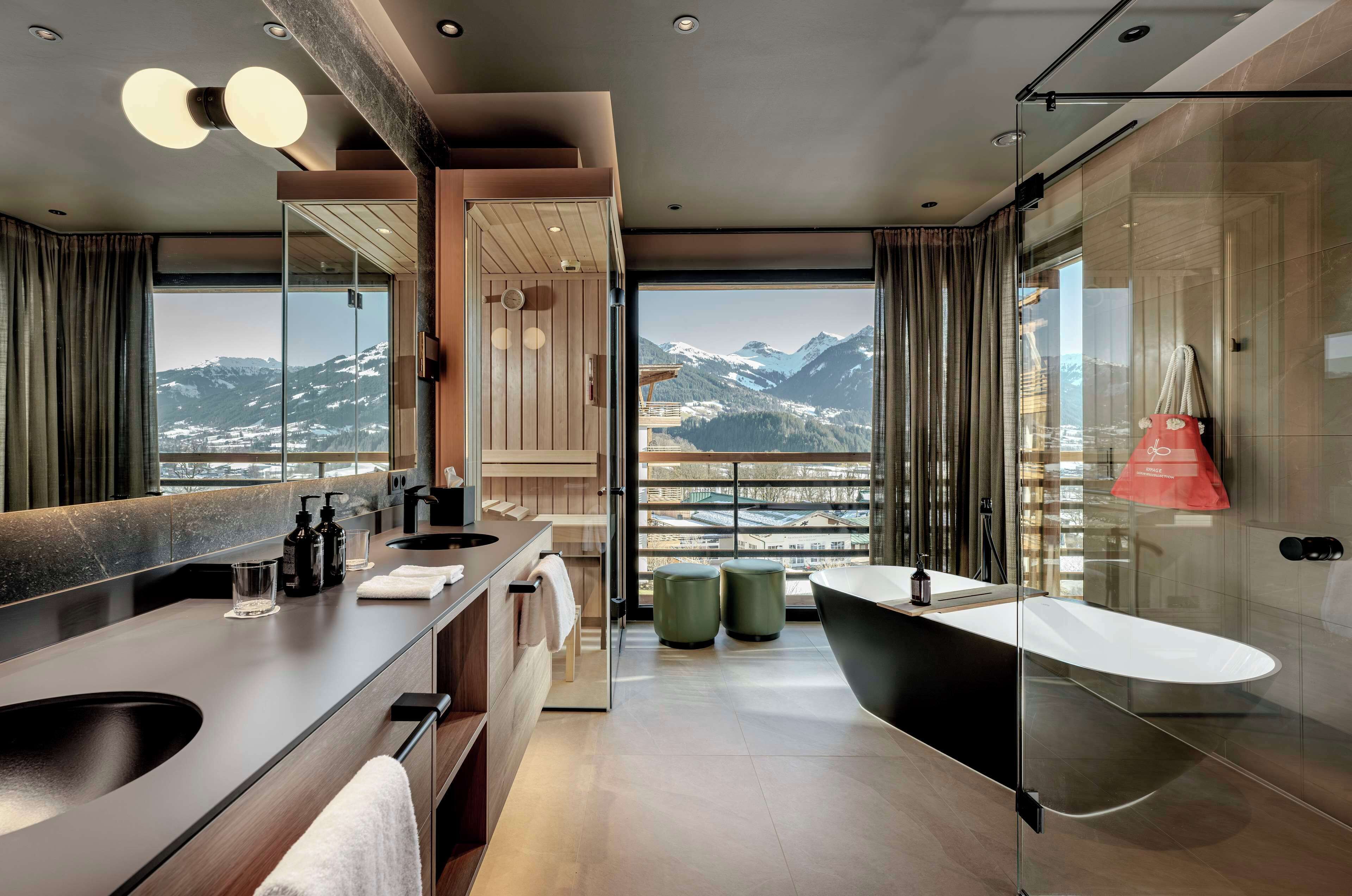 A modern bathroom with a large mirror, two sinks, a bathtub, and a view of snow-capped mountains.