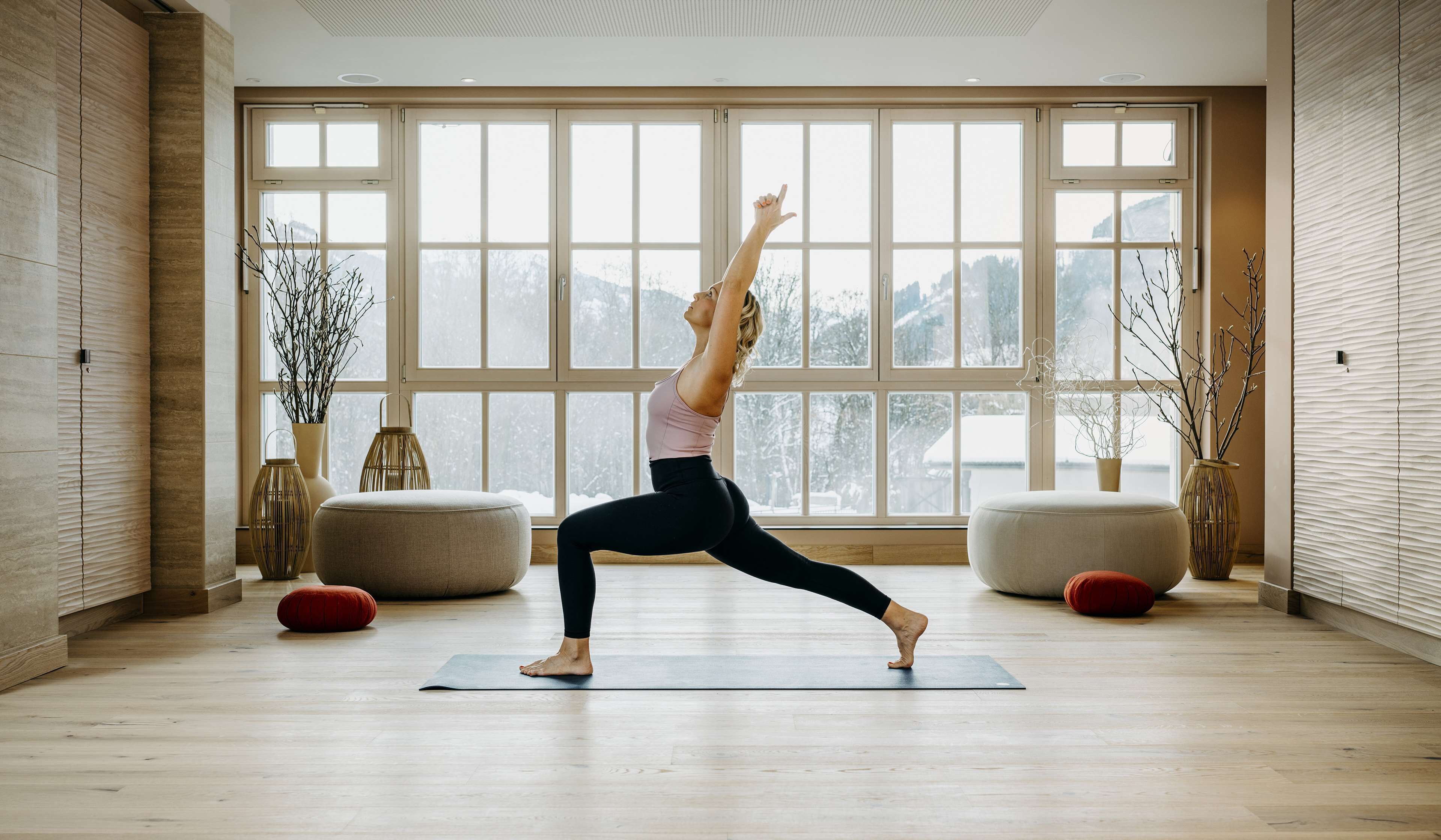 A spacious room with large windows, a yoga mat, and two ottomans.
