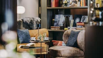 Un rincón acogedor para leer con un sillón cómodo, una mesita auxiliar con un libro y una taza, y una estantería llena de libros y objetos decorativos.