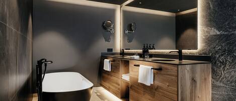 Un baño moderno con una bañera independiente, tocador de madera y un espejo grande.