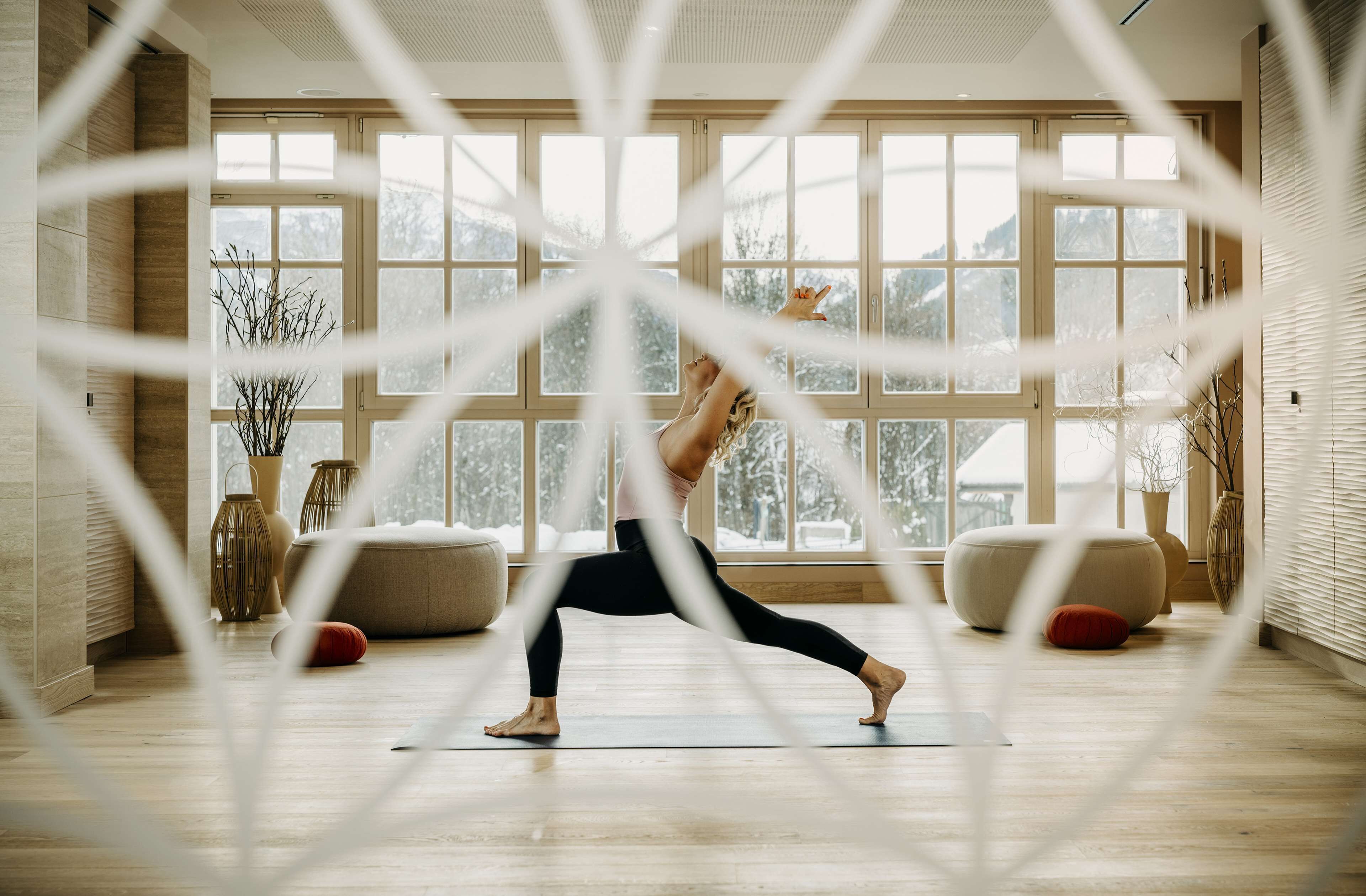 Una habitación amplia con ventanas grandes, piso de madera y una colchoneta para yoga.