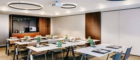 A conference room with multiple tables, chairs, and a projector.