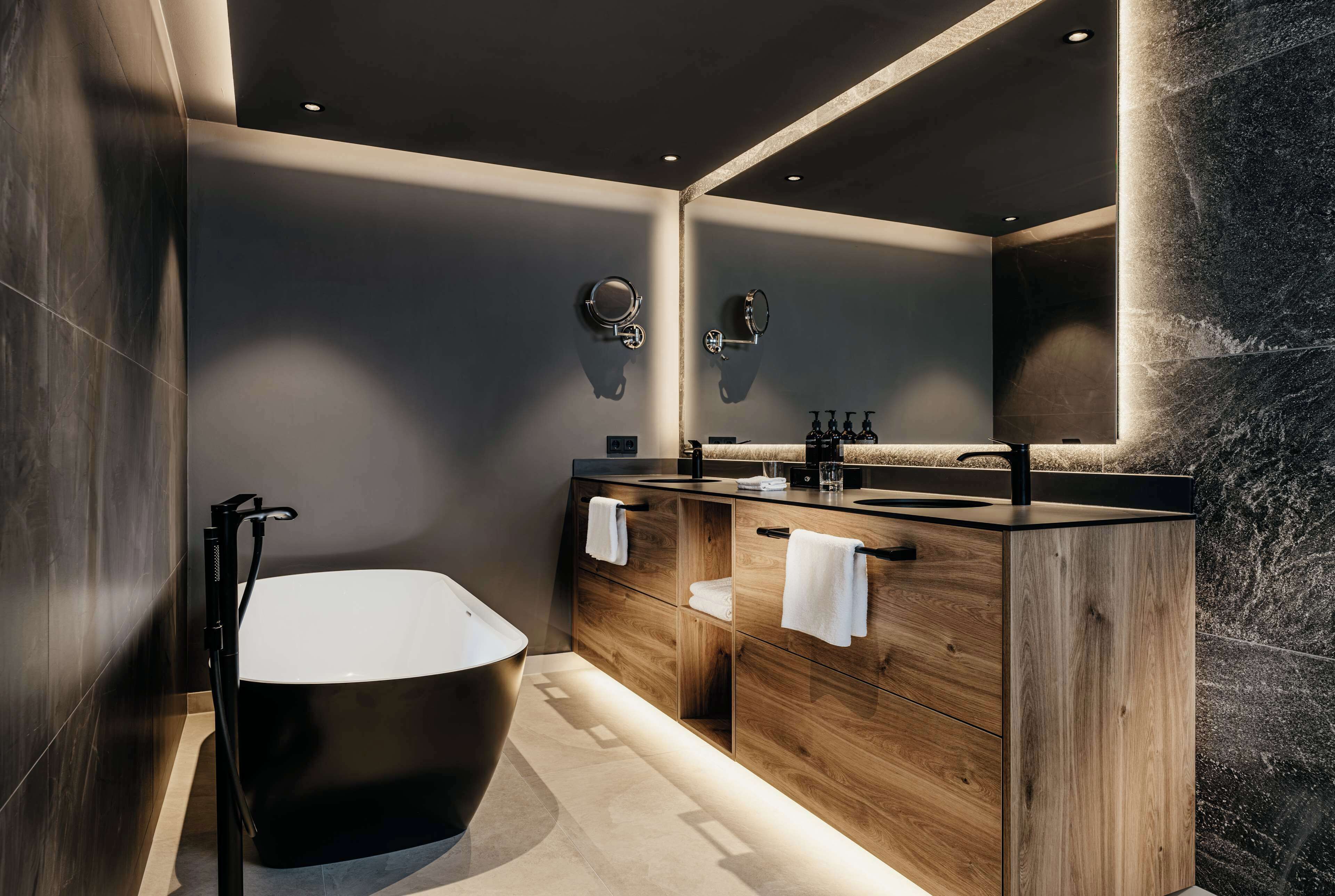 A modern bathroom with a freestanding bathtub, wooden vanity, and a large mirror.