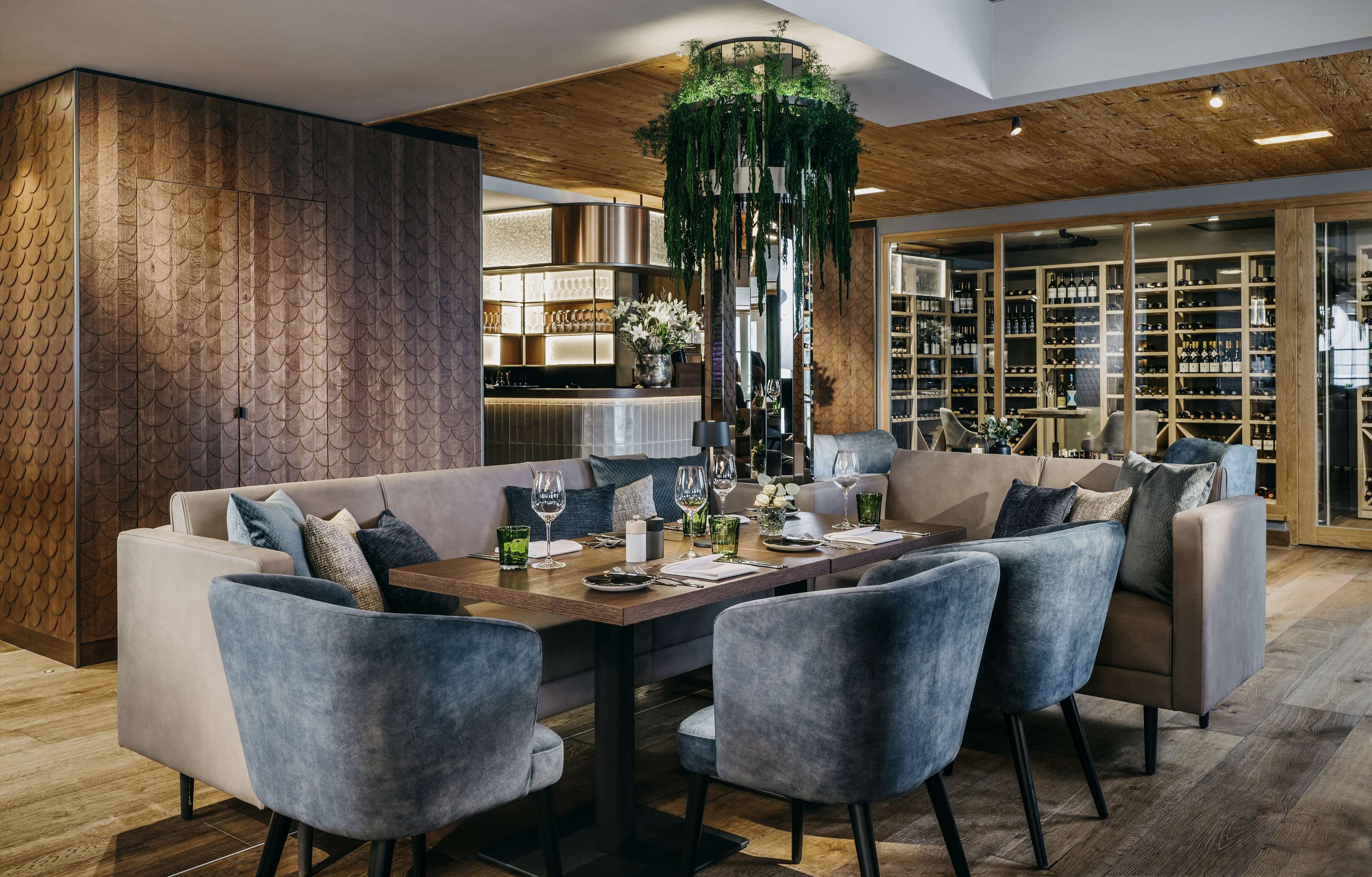 A modern dining area with a wooden ceiling, a central table with chairs, and a wine rack in the background.