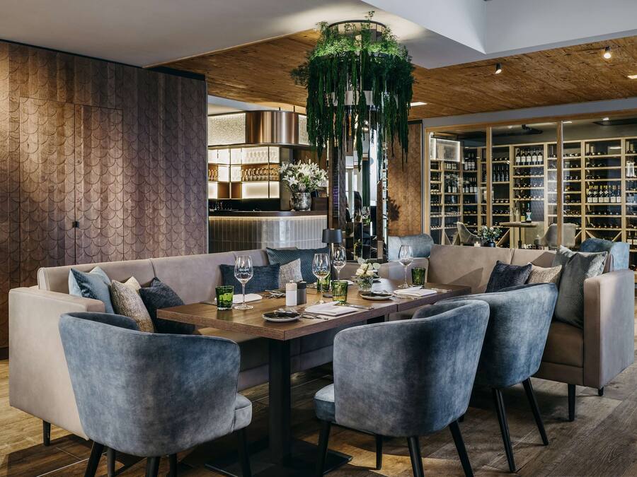 A modern dining area with a wooden ceiling, a central table with chairs, and a wine rack in the background.