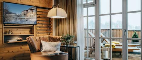 A cozy living room with a leather armchair, a small side table with a plant, and a large window with a view of a deck and outdoor furniture.