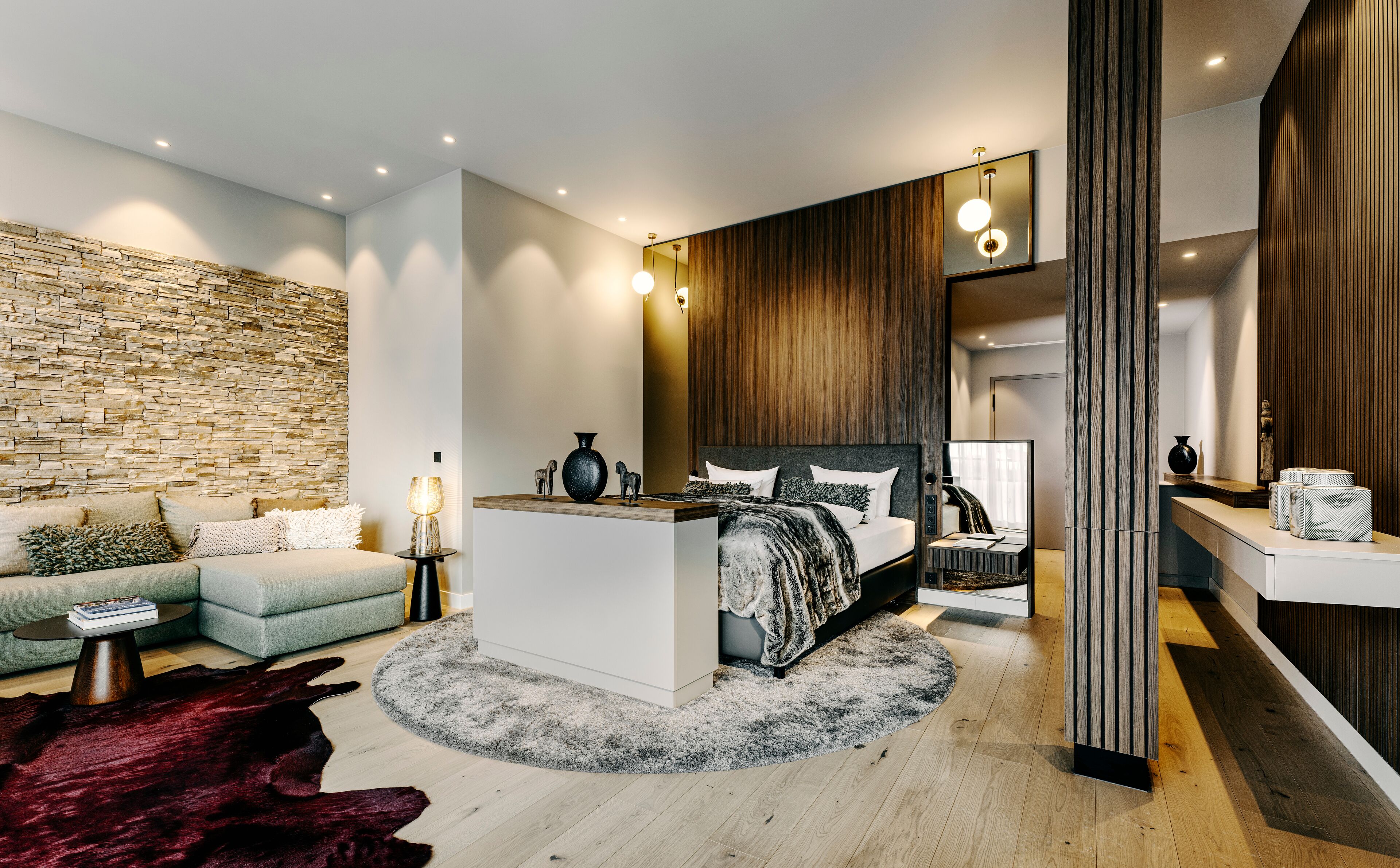Een moderne slaapkamer met een stenen muur, een bed met hoofdbord, een nachtkastje en een bureau met spiegel.