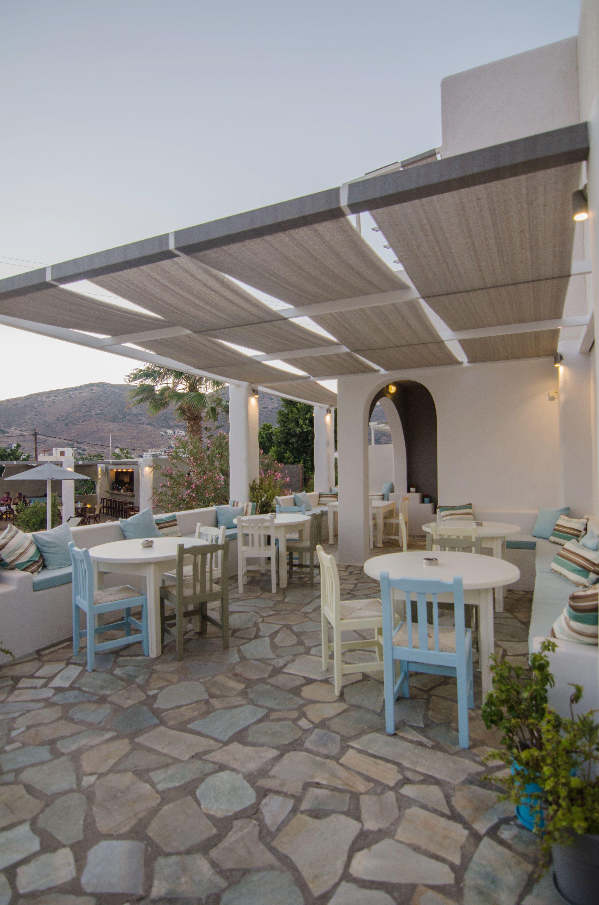 Un espace extérieur aménagé en terrasse, avec un sol en pierre, des meubles blancs et bleus, et une vue sur le paysage.