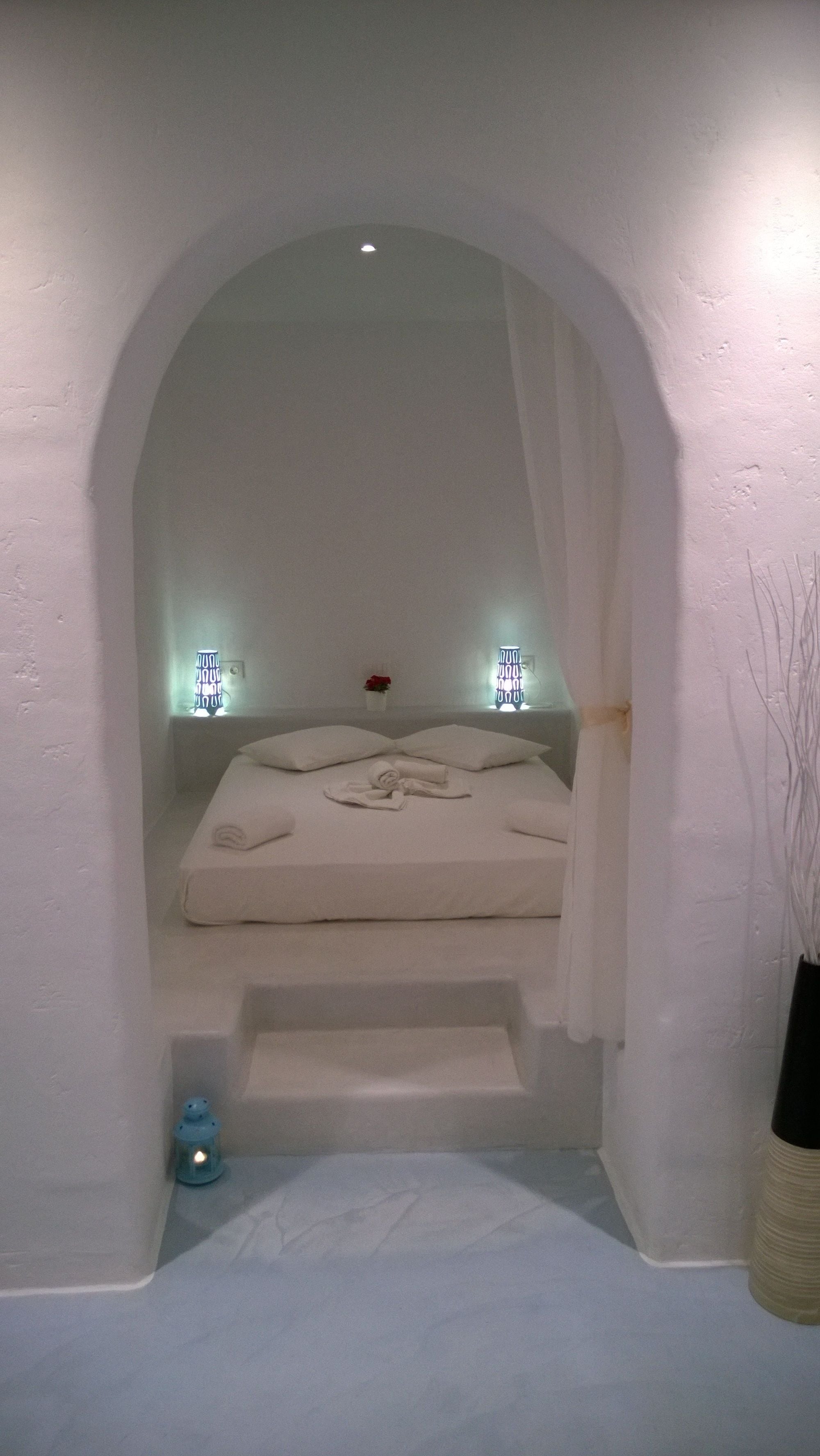 Un dormitorio acogedor con arco, una cama, dos lámparas de noche y una mesita con un jarrón de flores.