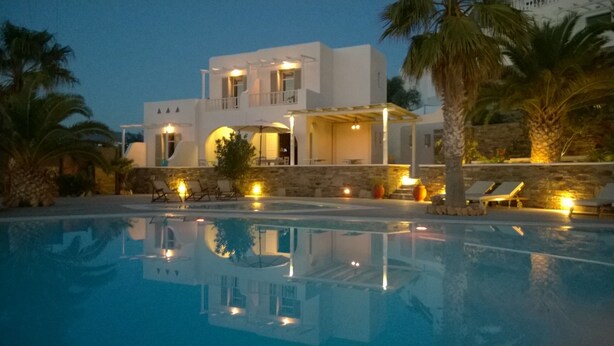 A modern villa with a swimming pool, outdoor seating, and a stone wall. - Olga's Pension (Ios)