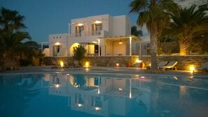A modern villa with a swimming pool, outdoor seating, and a stone wall. - Olga's Pension (Ios)
