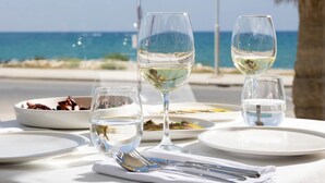 A table set with white plates, wine glasses, and cutlery, with a view of the sea and a palm tree in the background. -  Pearl SeaBreeze Suites (Rethymno)