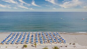 A beach with rows of blue umbrellas and sun loungers, a clear sky, and the ocean in the background. -  Pearl SeaBreeze Suites (Rethymno)