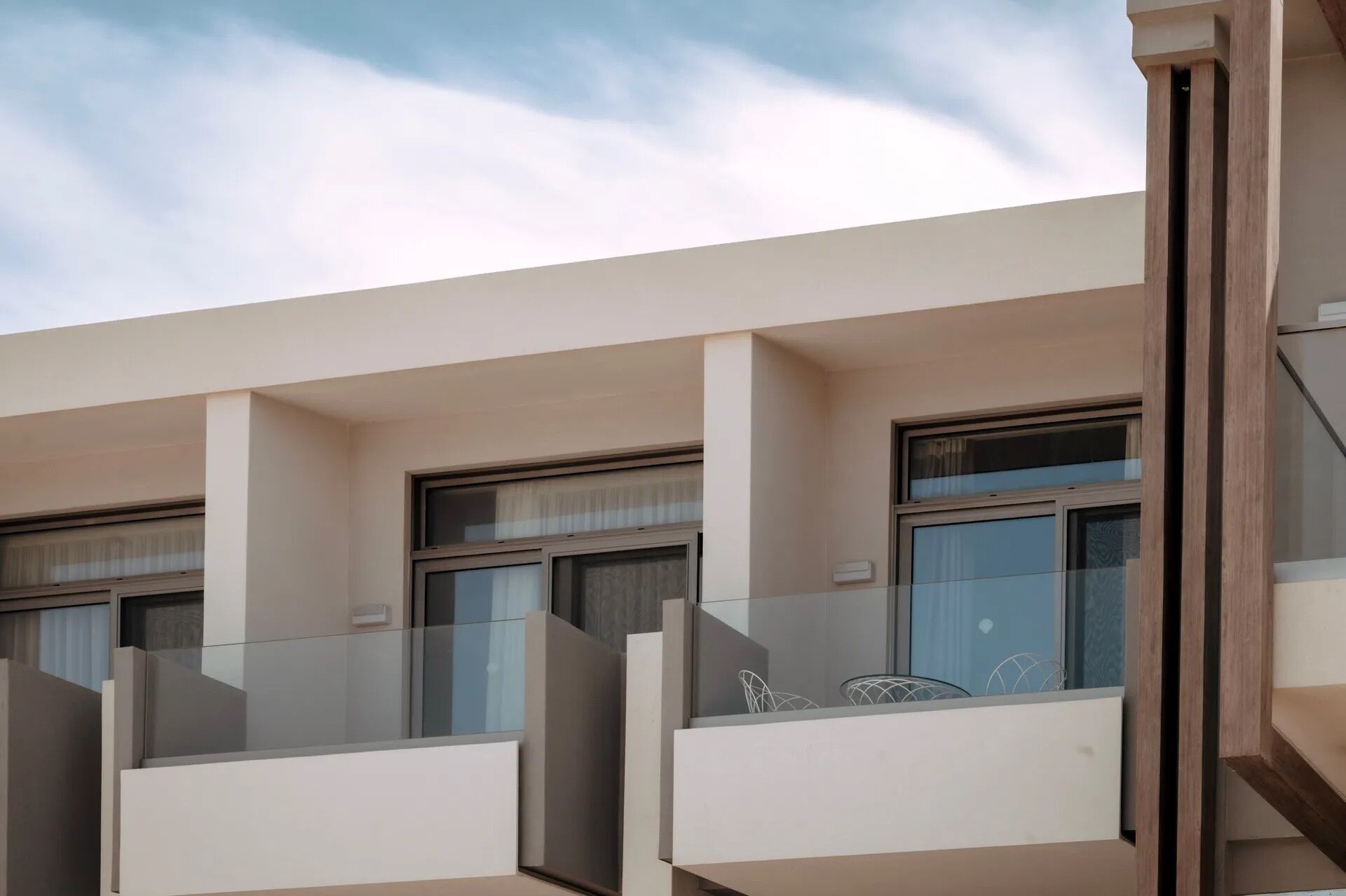 A modern building with multiple balconies, each with a glass railing and a view of the sky.