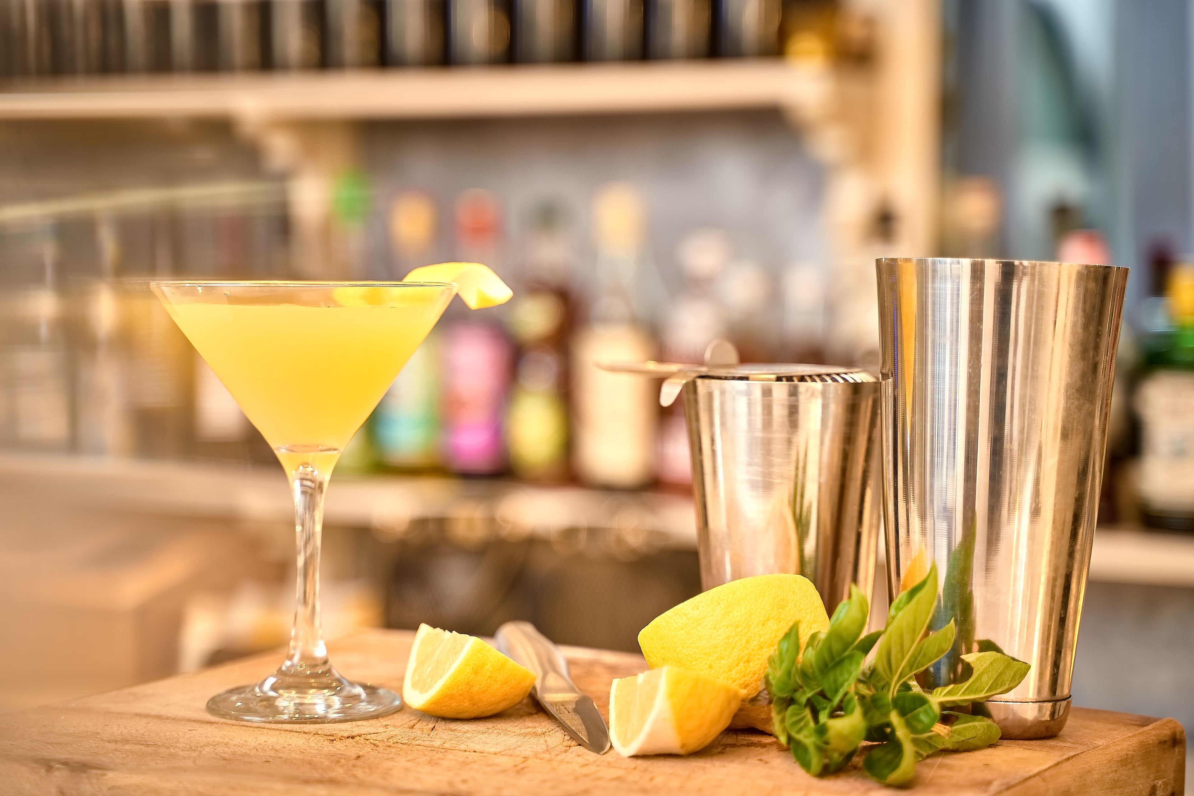 Una copa de martini con una rodaja de limón sobre una superficie de madera, junto a una coctelera y un trozo de limón.