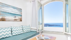 Una habitación con vistas al mar, un sofá con cojines estampados, una mesa de madera con un libro y un cuadro en la pared.