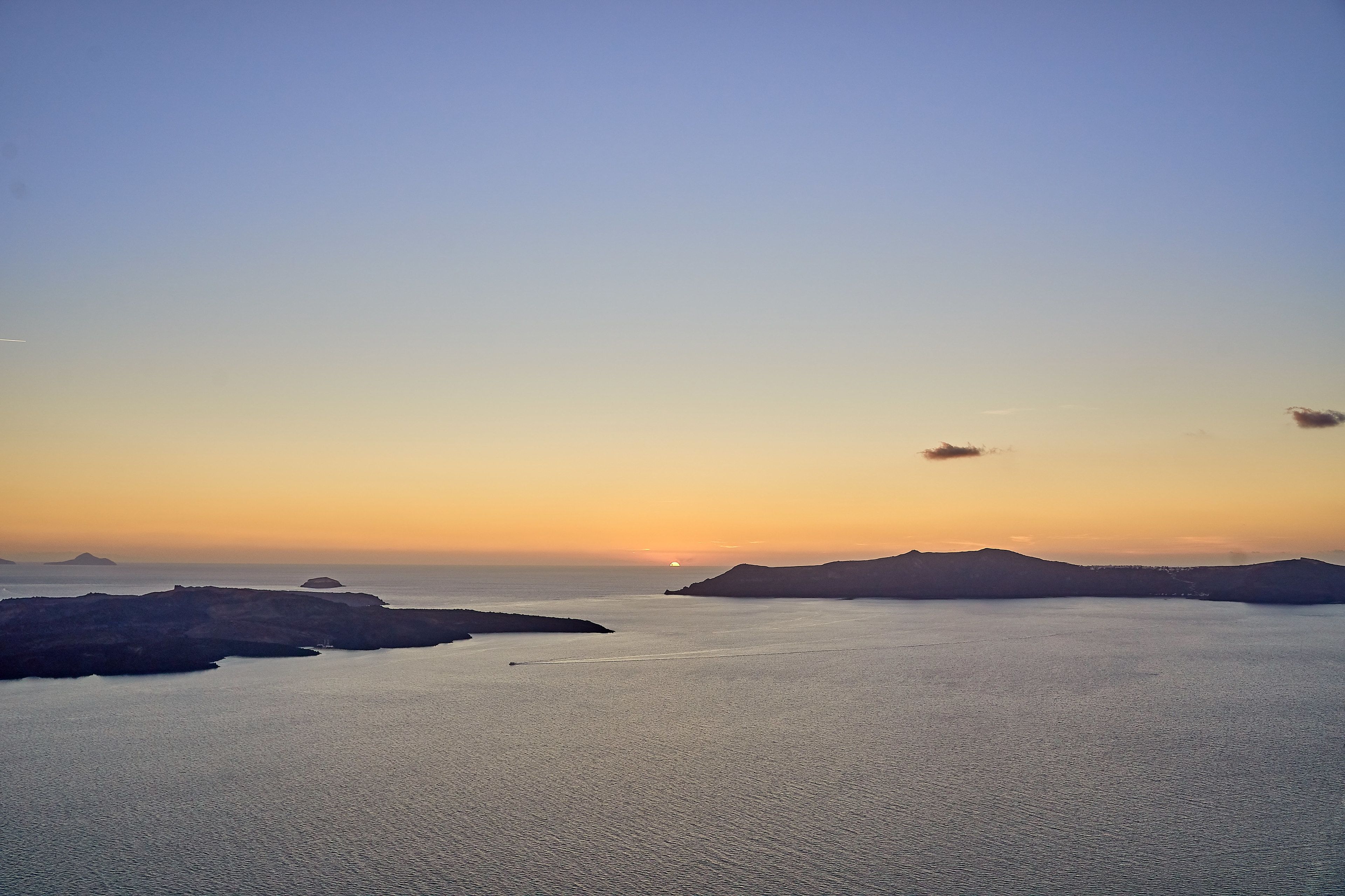 A coastal landscape with a sunset over the sea, featuring rocky outcrops and distant islands.