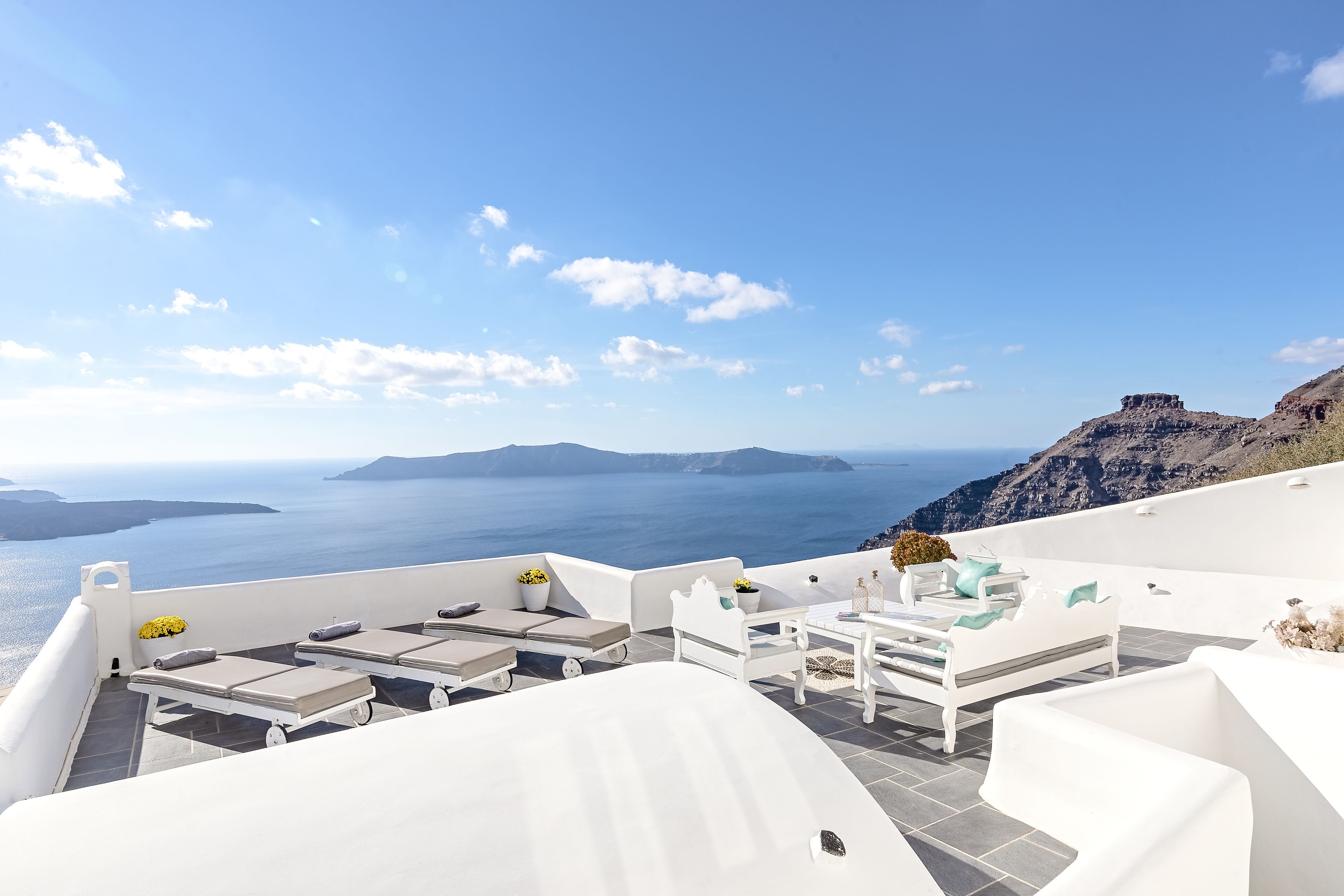 A white outdoor seating area with a view of the sea and islands.