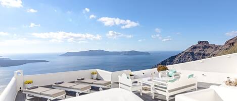 A white outdoor seating area with a view of the sea and islands.