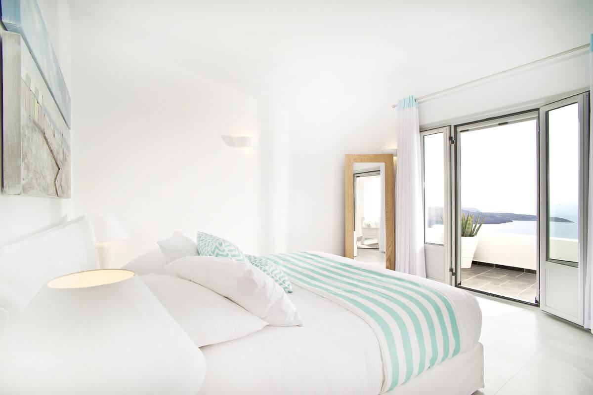 Quarto moderno com uma cama grande, uma mesa de cabeceira e vista para o mar através de uma porta de vidro deslizante.