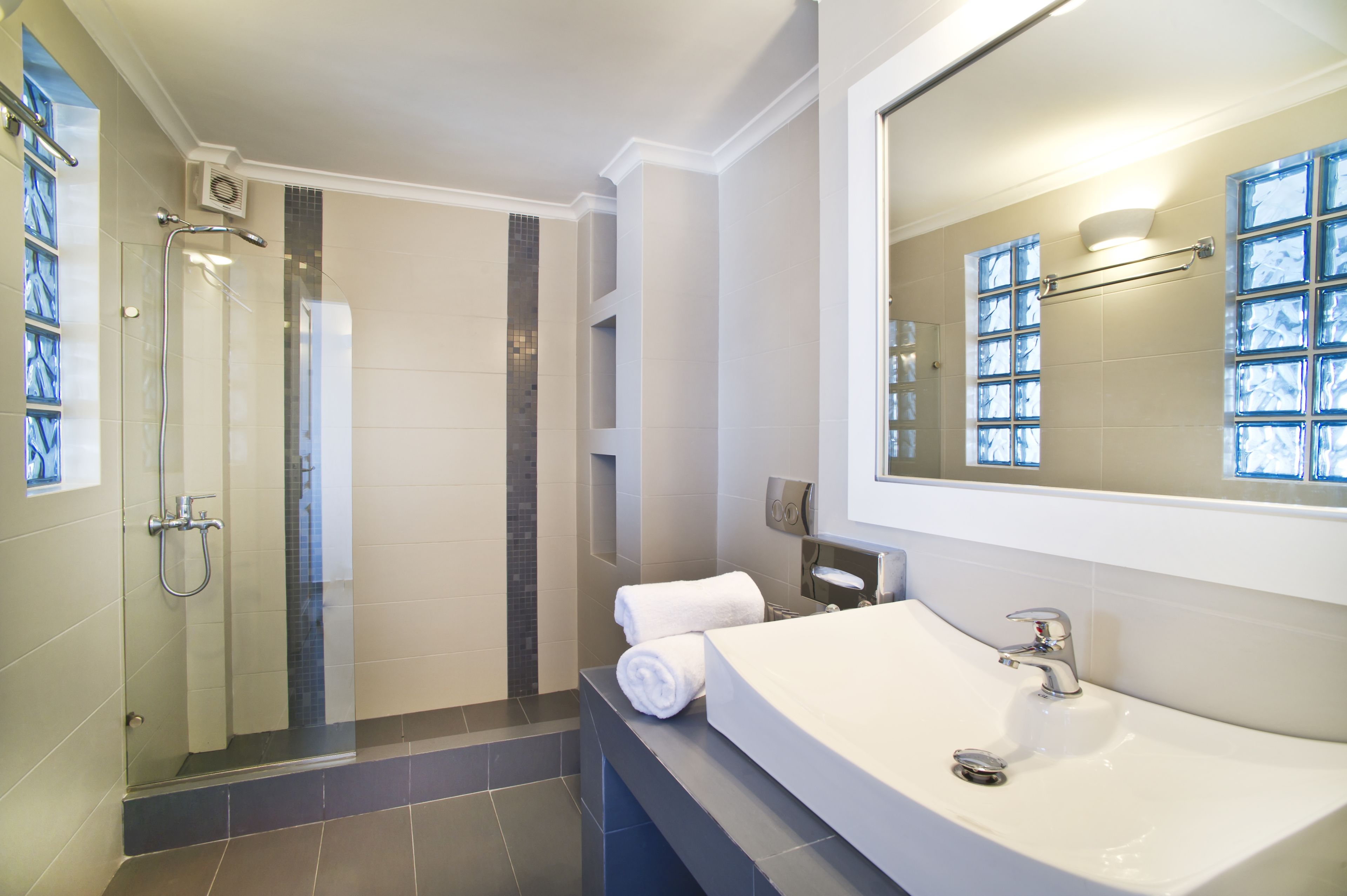 A modern bathroom with a glass-enclosed shower, a large mirror, and a white sink.
