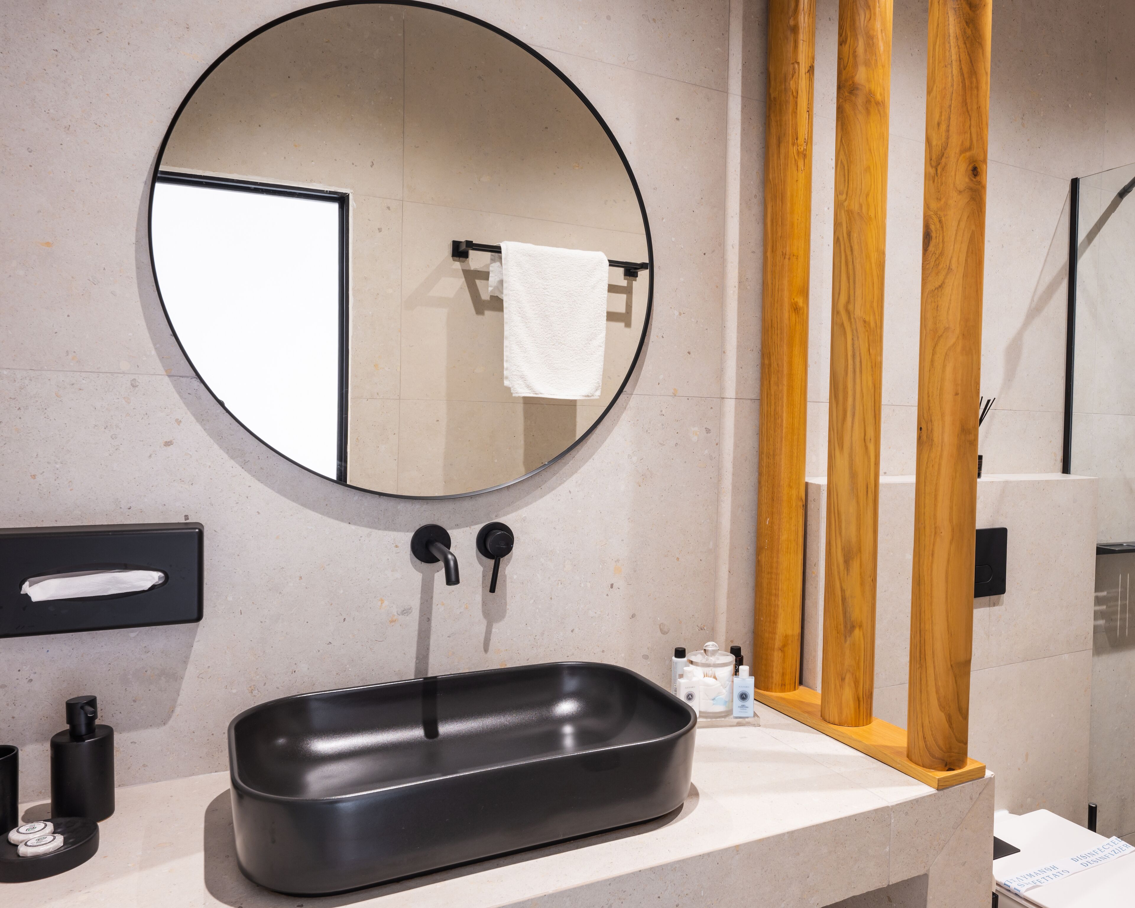 A modern bathroom with a round mirror, black sink, and wooden accents.