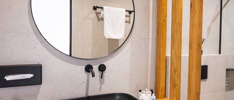 A modern bathroom with a round mirror, black sink, and wooden accents.