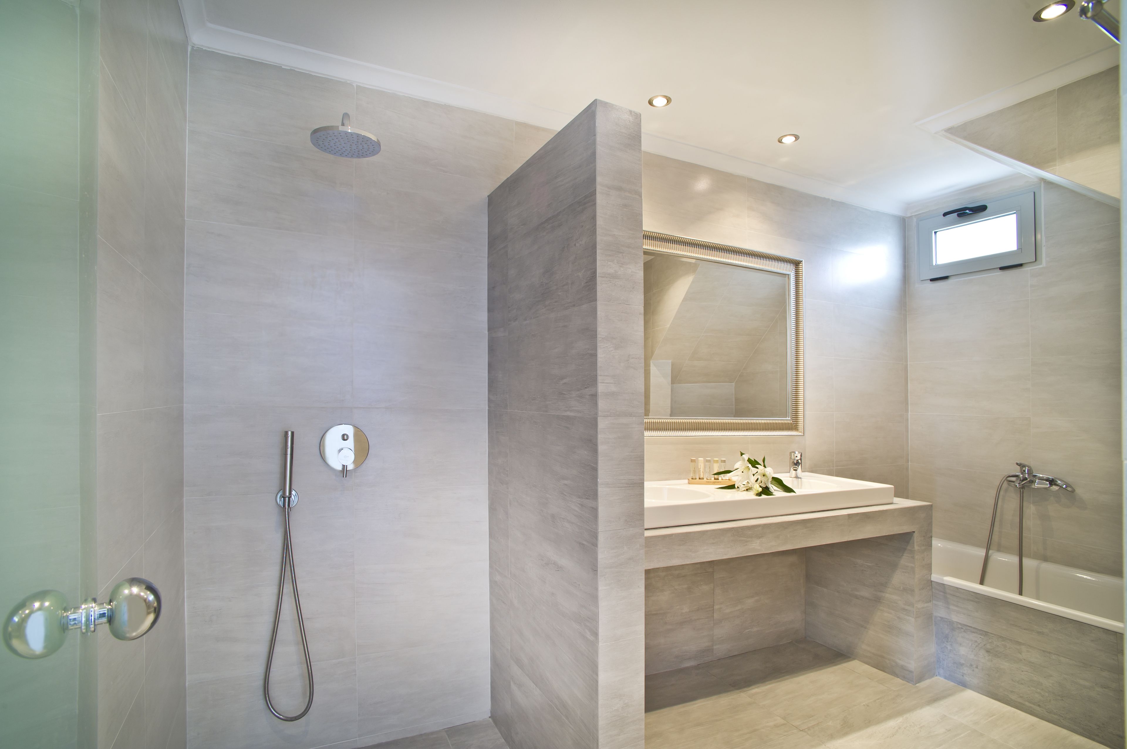 Ein modernes Badezimmer mit barrierefreier Dusche, einem Waschtisch mit Spiegel und einer Badewanne.