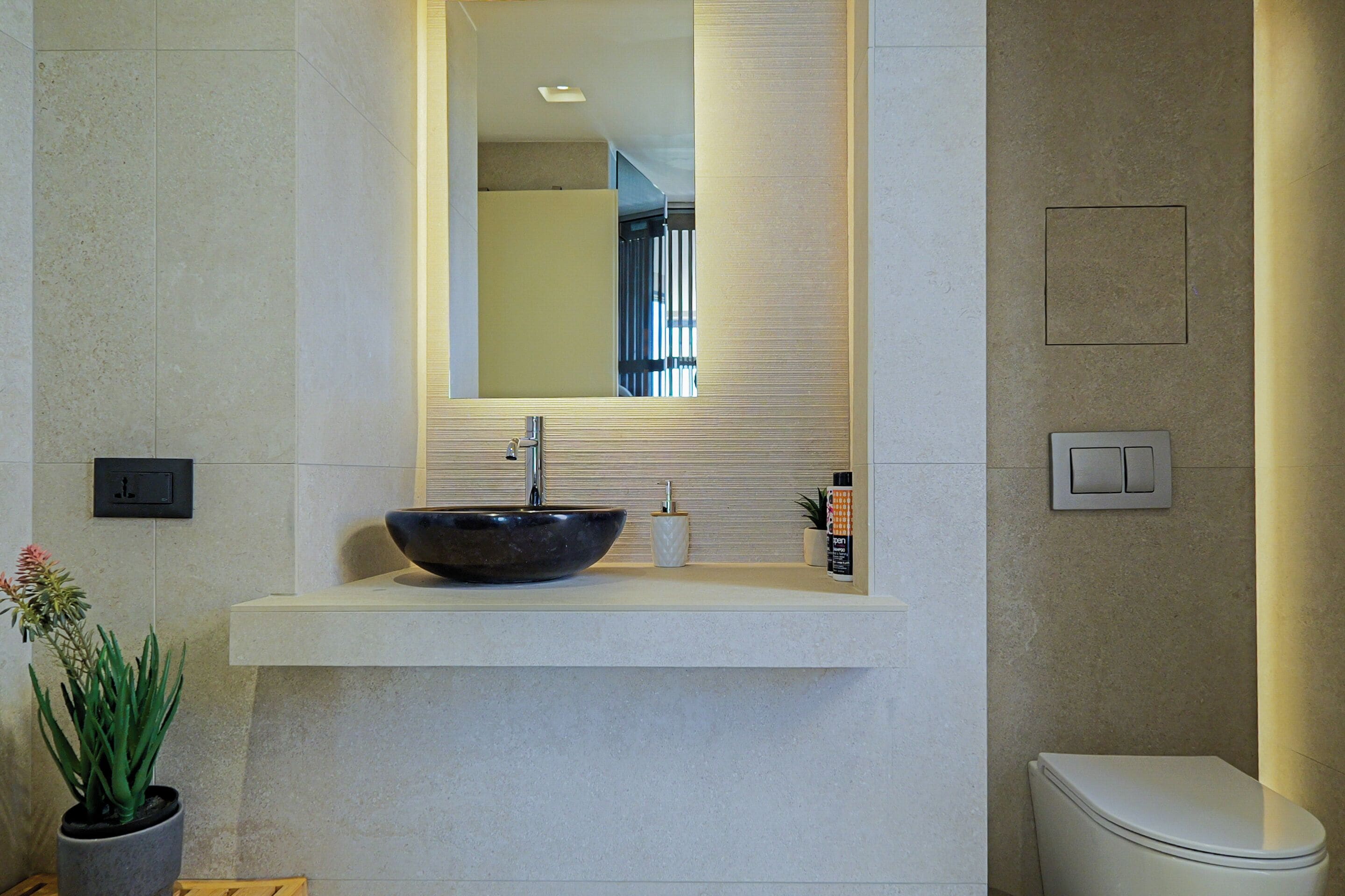 Un baño con lavabo sobre encimera, espejo, inodoro y planta en maceta.