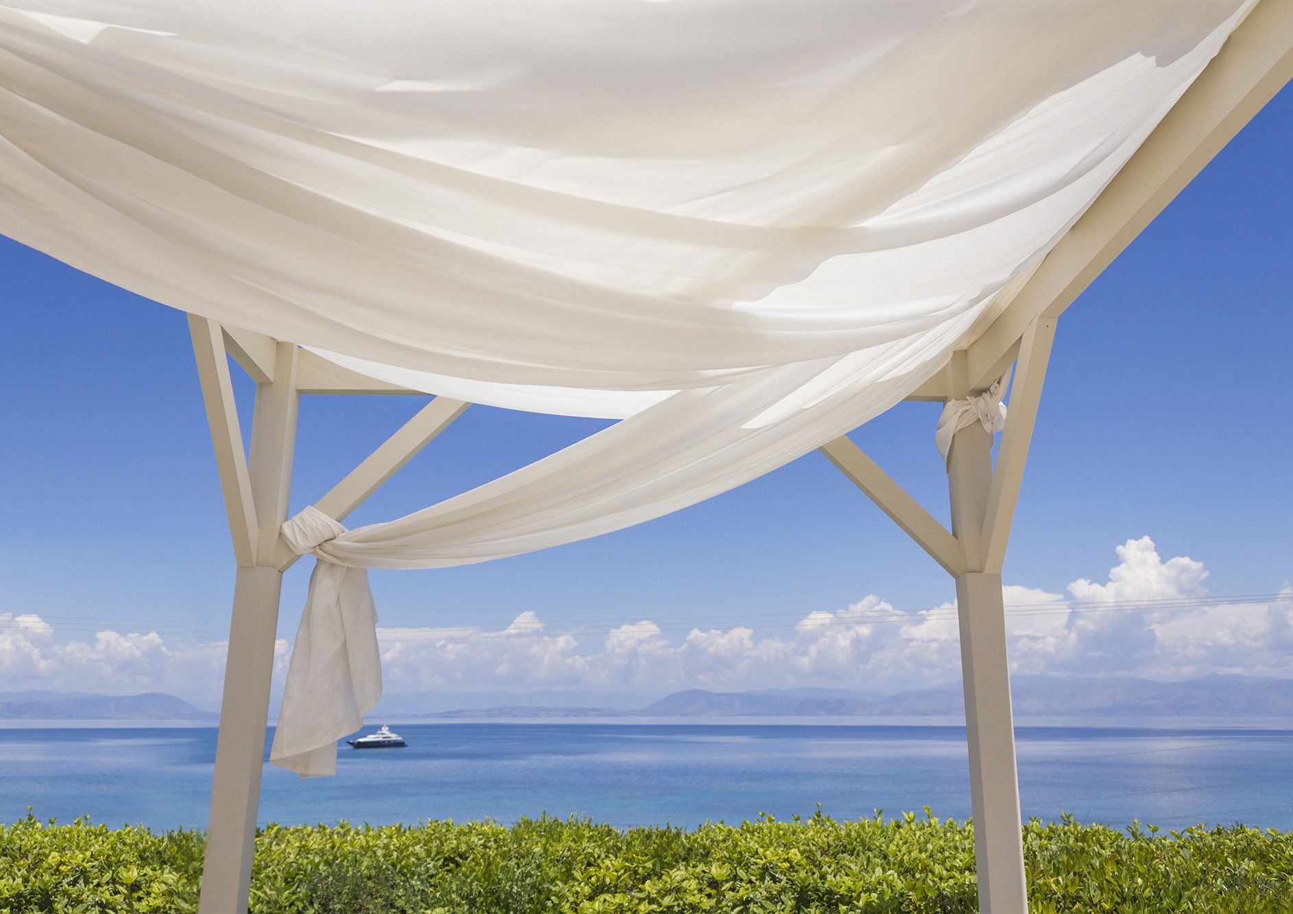 A white gazebo with a view of the sea and a yacht in the distance.