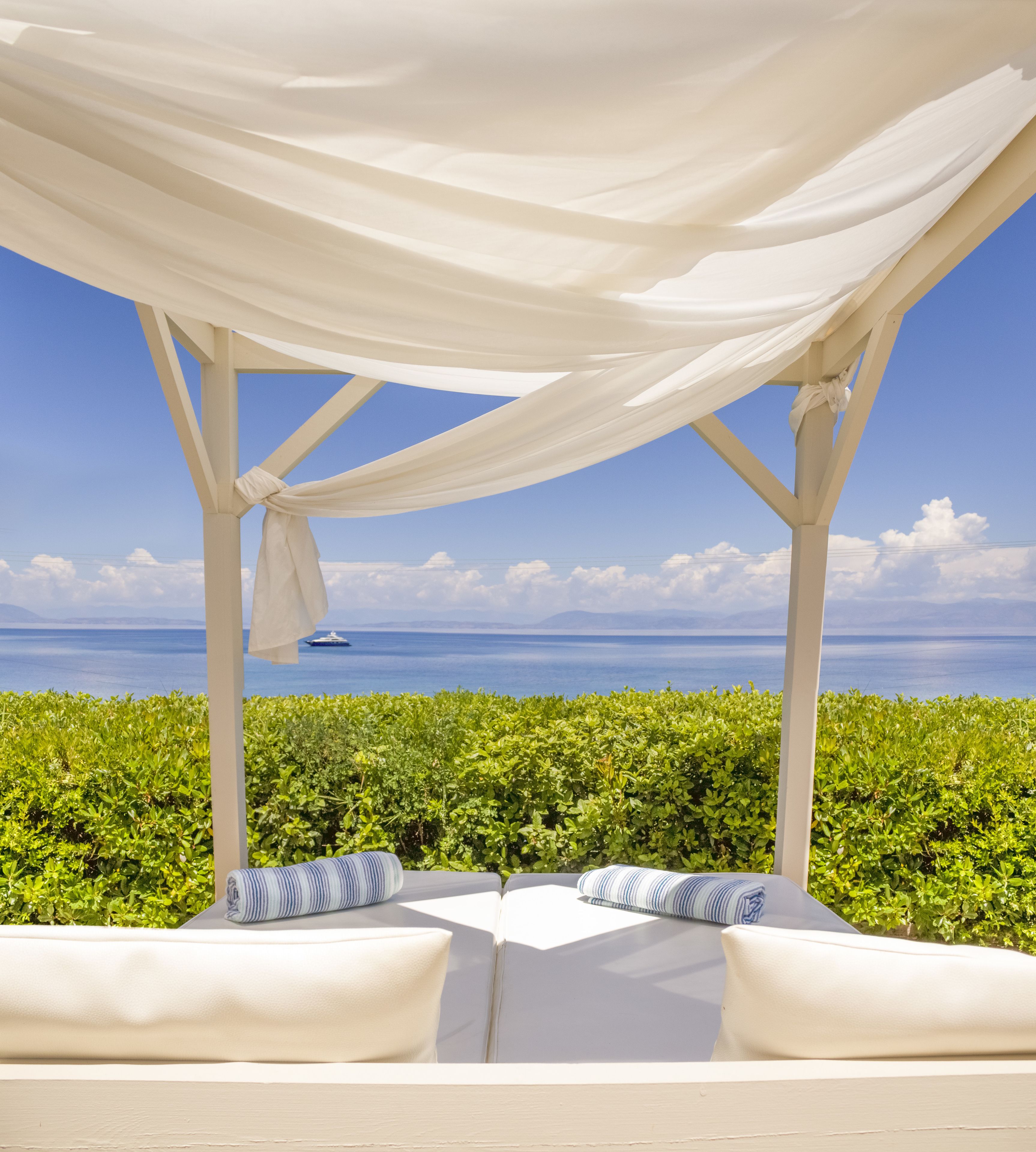 A covered outdoor seating area with white cushions and a view of the sea.