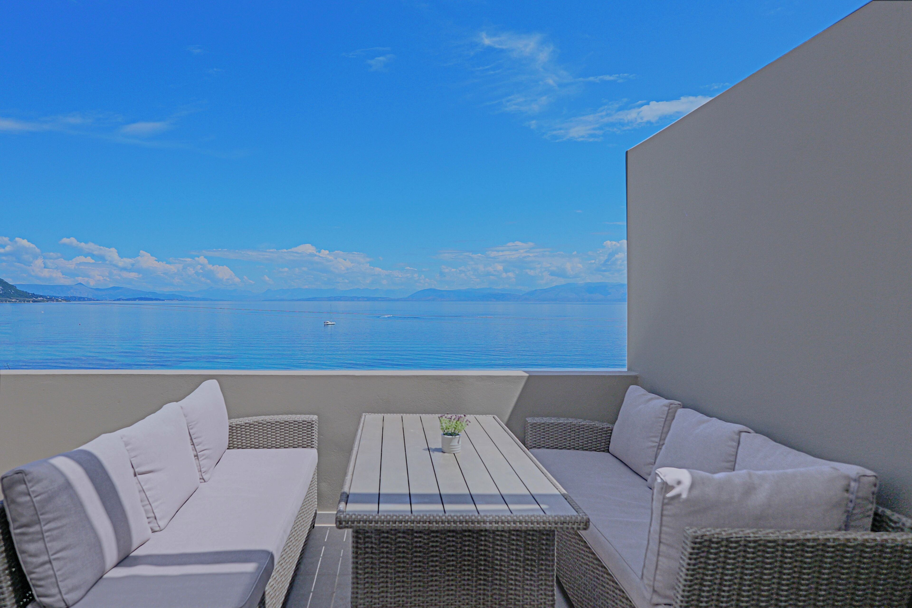 A balcony with wicker furniture, a small table, and a view of the sea.