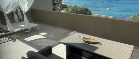 A balcony with a view of a coastal town, a table with a woven basket, and a white canopy.