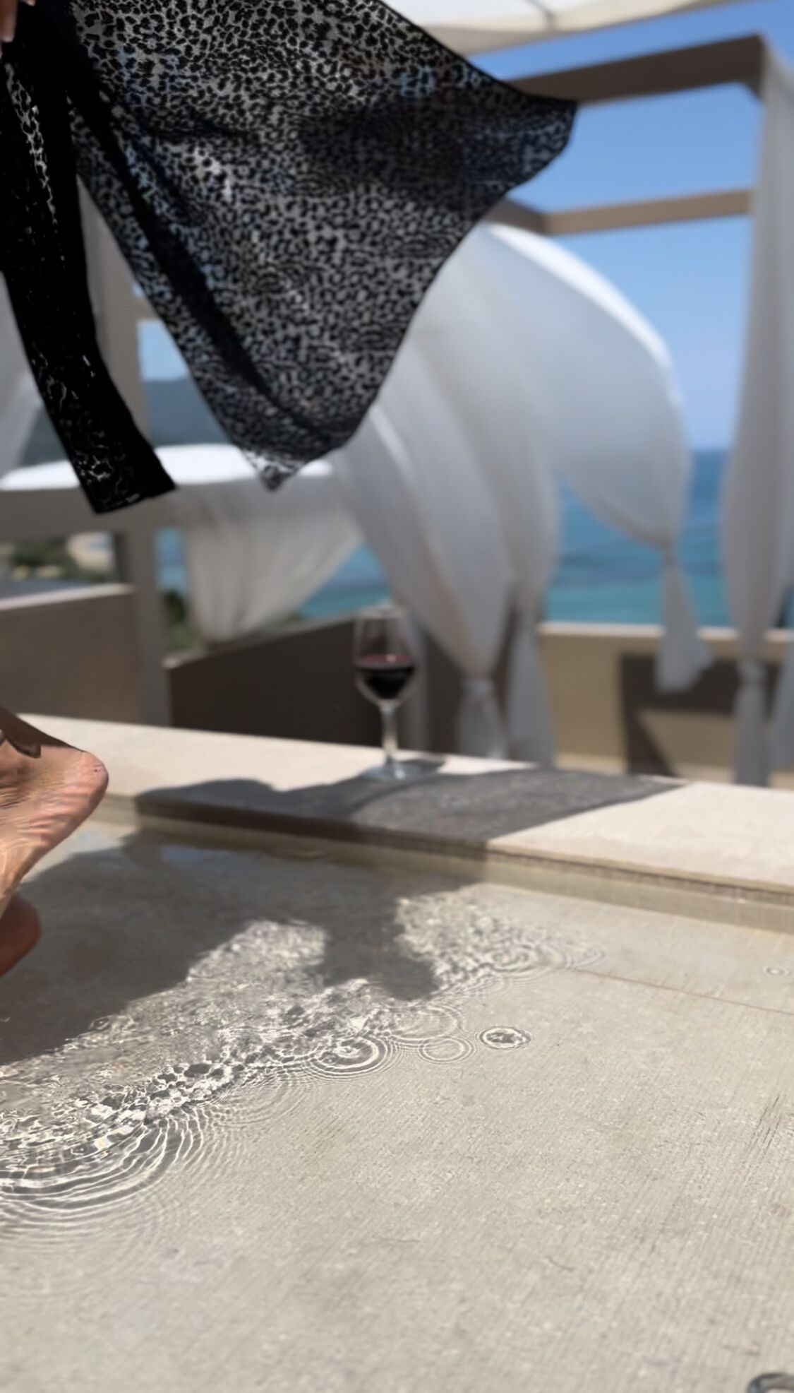 Un gros plan d’une table sur laquelle on aperçoit un verre de vin rouge, une nappe blanche et un tissu à motifs qui est drapé sur la table.