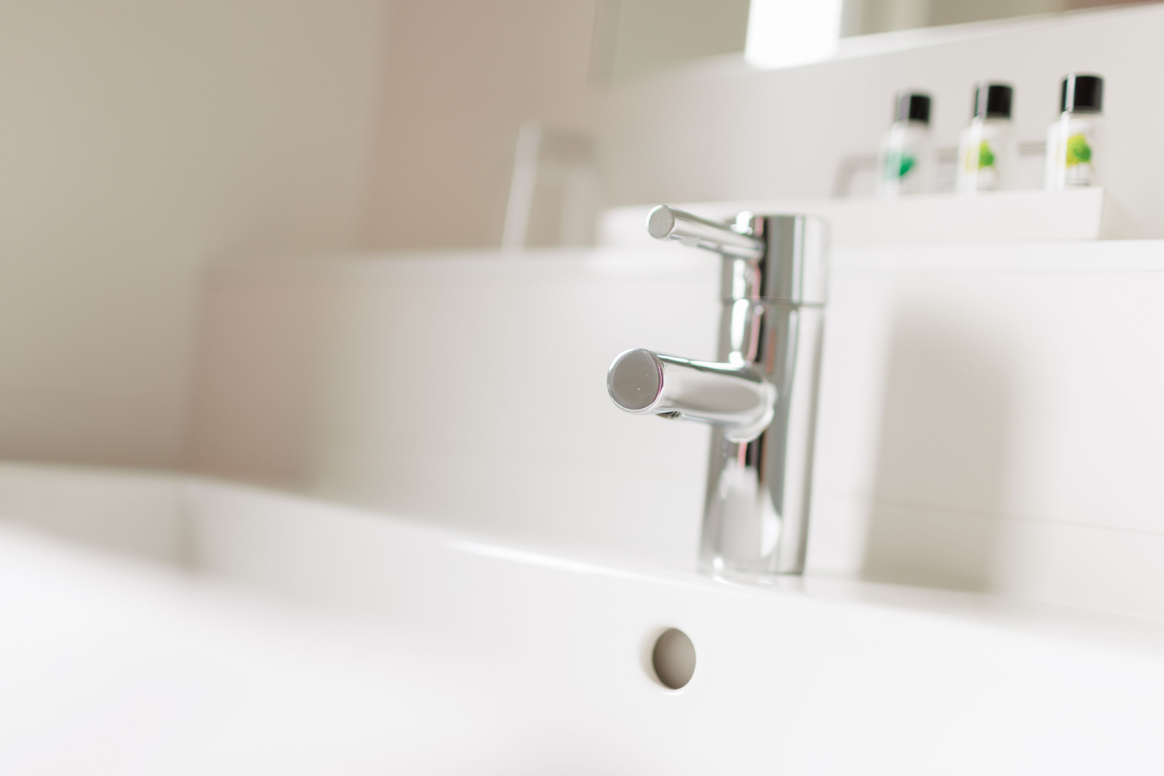 A modern bathroom with a chrome faucet, a white sink, and a mirror above it.