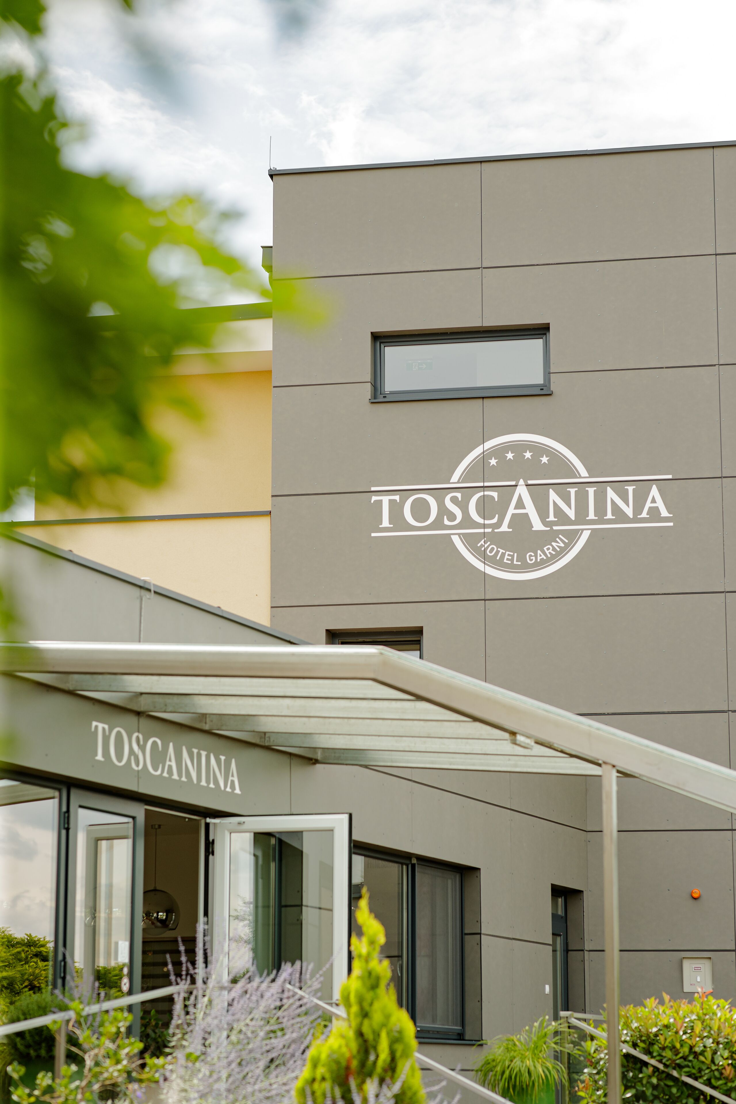 The exterior of the Toscana Hotel with a clear view of the entrance and the hotel's name on the facade.