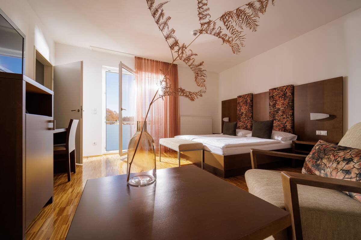 Ein modernes Hotelzimmer mit Bett, Schreibtisch, Stuhl, Sofa und einer Zimmerpflanze.