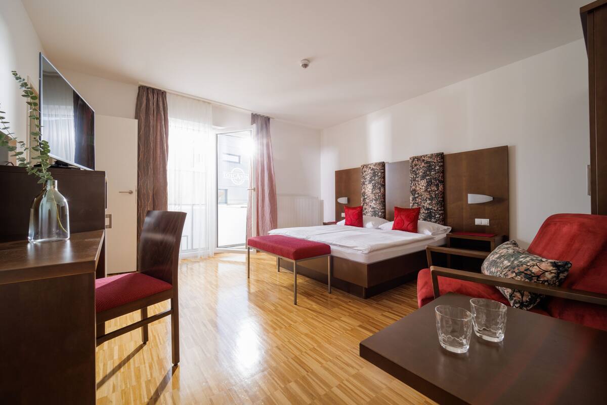 Ein Hotelzimmer mit einem Bett, einem Schreibtisch, einem Sessel, einer Couch und einem Fernseher.