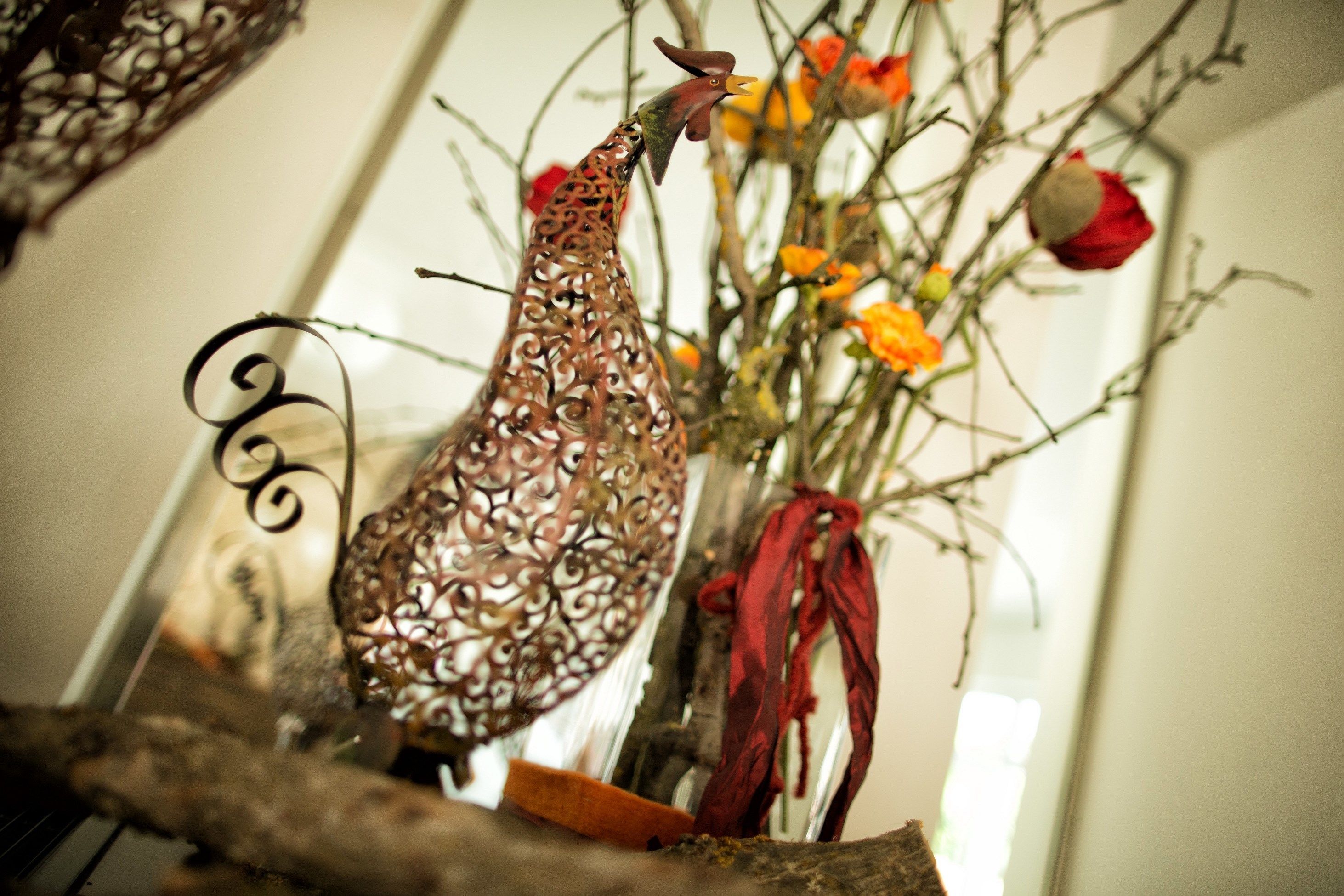 Un gallo decorativo en un florero de vidrio con flores y un lazo rojo.