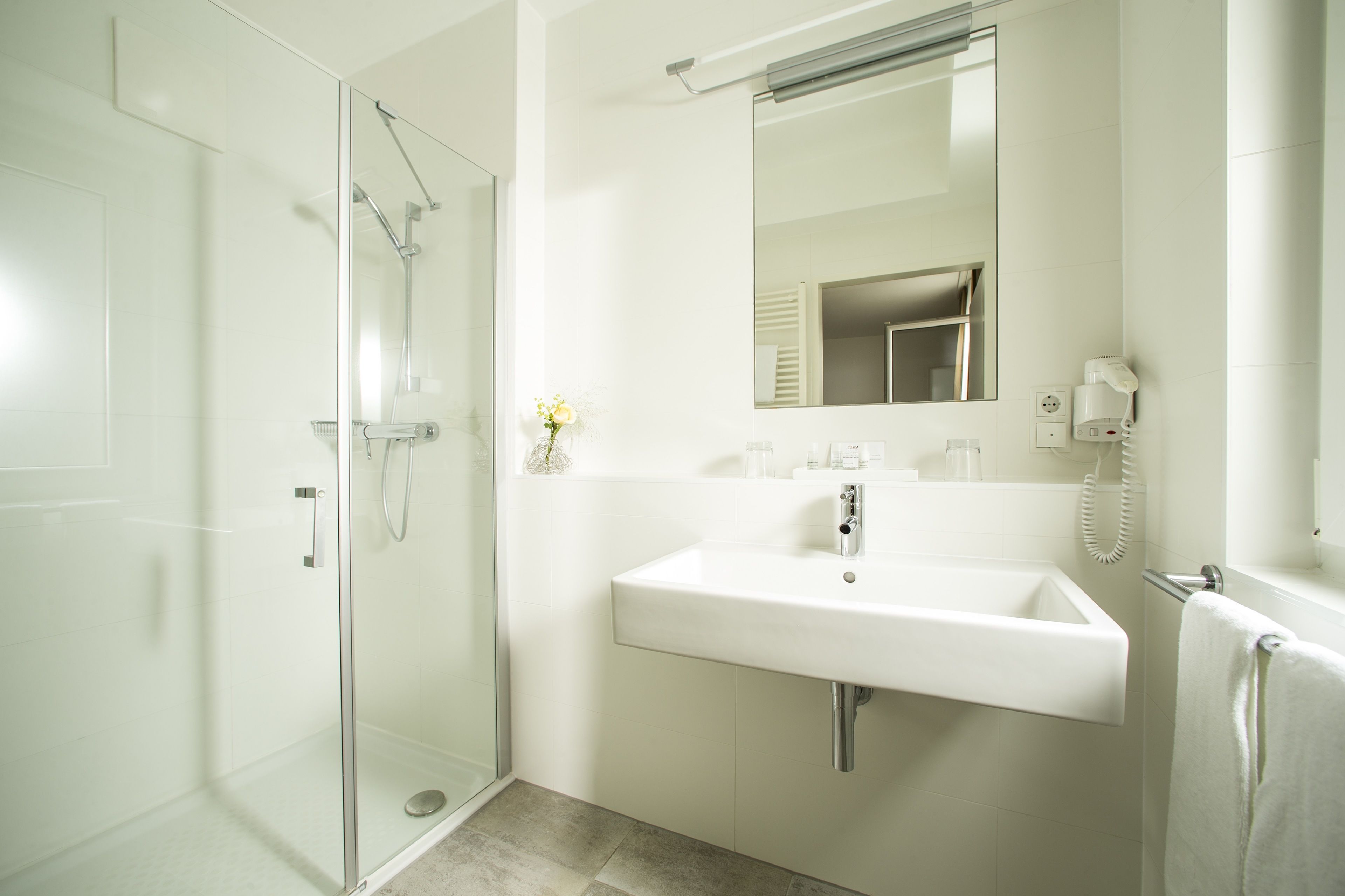A modern bathroom with a glass-enclosed shower, a white sink, and a mirror above it.