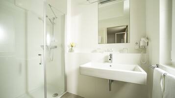 A modern bathroom with a glass-enclosed shower, a white sink, and a mirror above it.