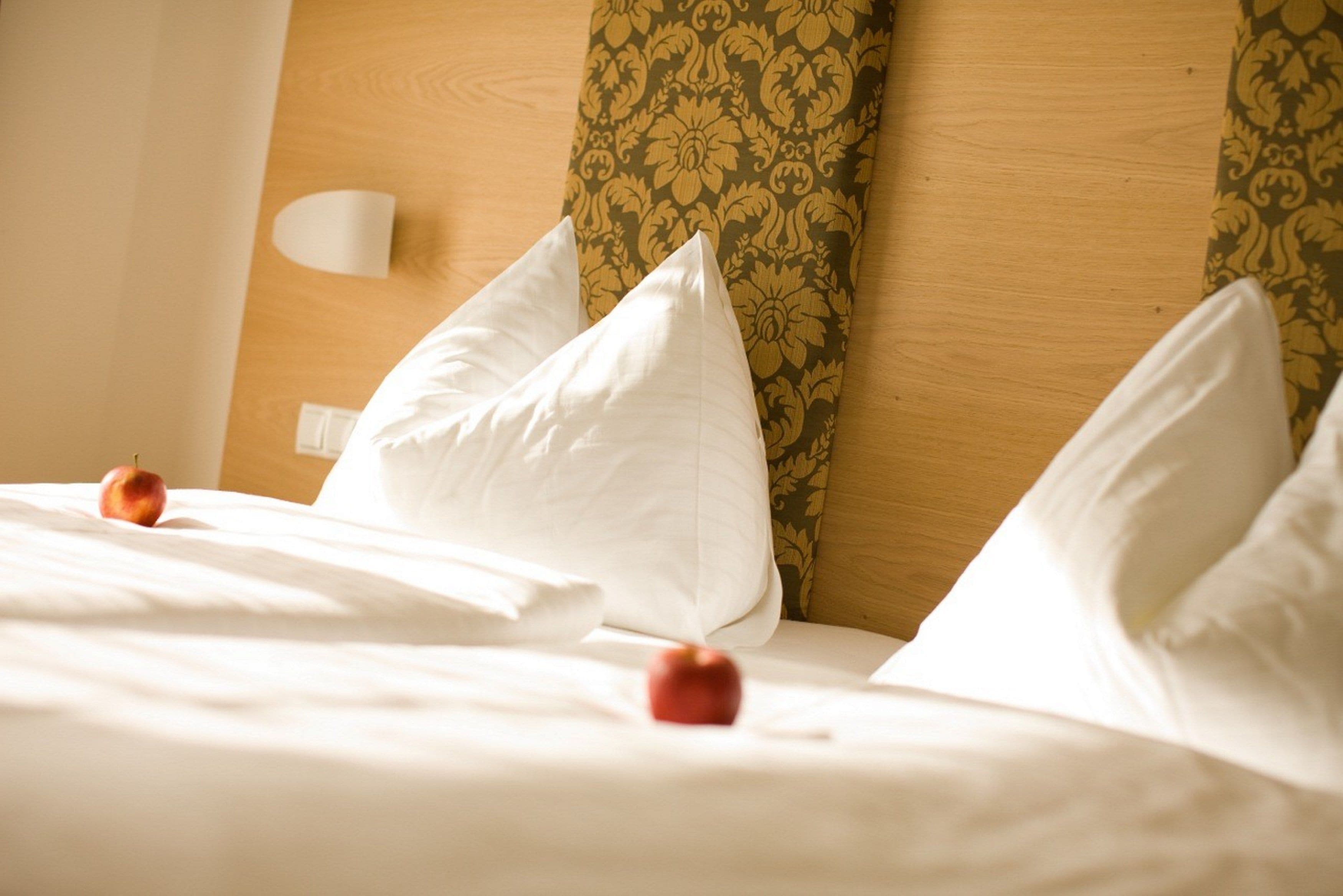 A neatly made bed with white pillows and a single apple on the bed.